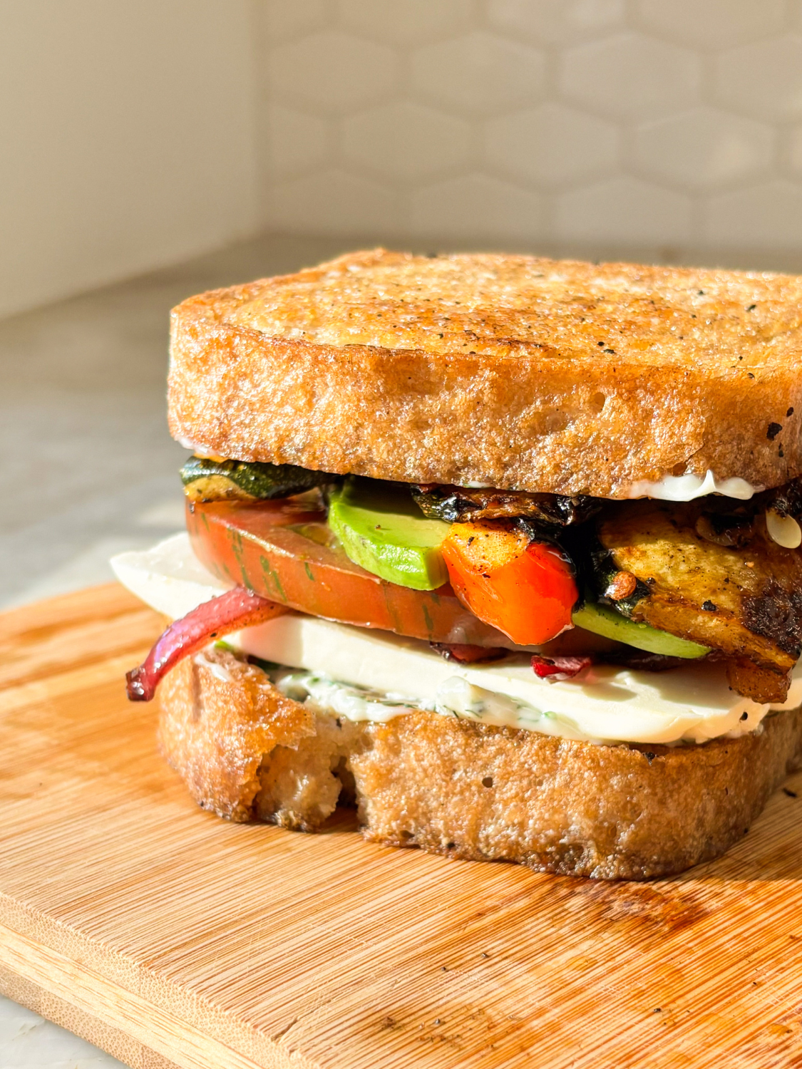 Toasted thick slices of Classic Bread SRSLY loaf made into a sandwich with mozzerella, tomato, red onion, chicken, and avocado