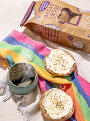 Bread SRSLY gluten-free sourdough sandwich rolls topped with cream cheese and bagel seasoning next to a steaming cup of coffee.