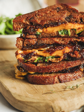 Load image into Gallery viewer, Stack of cinnamon raisin grilled cheese sandwiches on a wooden cutting board with a blurred background