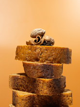 Load image into Gallery viewer, Stack of sliced pumpkin spice bread with spices on top with an orange background